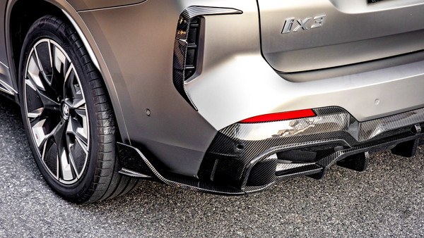 Car with "iX3" badging, featuring a sleek rear bumper and carbon fiber diffuser, parked on a paved surface. The rear wheel has a modern rim design.