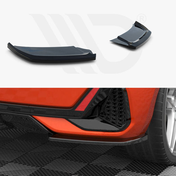 Two aerodynamic car accessories rest on a white surface, above a rear view of an orange car parked on a checkered floor, highlighting the vehicle's sleek design and wheels.