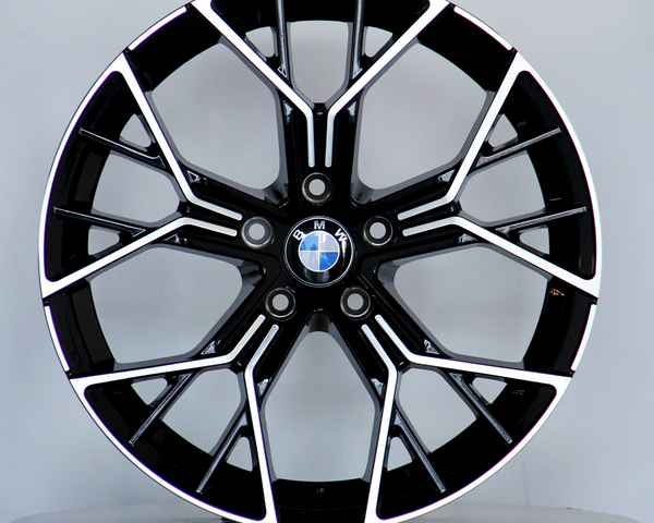 A black and silver BMW alloy wheel, featuring a multi-spoke design, is displayed upright on a light gray circular platform. The BMW logo is centered.
