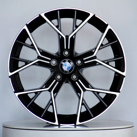 A black and silver BMW alloy wheel, featuring a multi-spoke design, is displayed upright on a light gray circular platform. The BMW logo is centered.