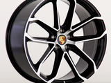 A black and silver alloy wheel features the Porsche emblem at the center, with a modern, multi-spoke design. The wheel is set against a plain, light background.