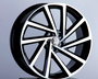 A black and silver alloy car wheel, featuring a Volkswagen logo at the center, is displayed upright on a pedestal against a plain, light gray background.