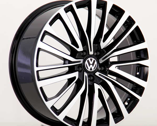 A black and silver alloy car wheel features a sleek, multi-spoke design with a Volkswagen logo at the center, positioned on a plain white background.
