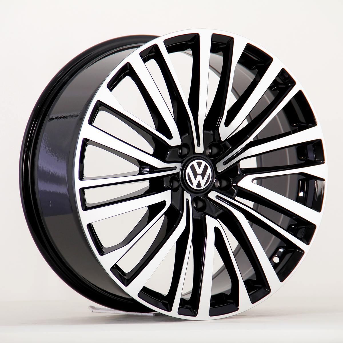 A black and silver alloy car wheel features a sleek, multi-spoke design with a Volkswagen logo at the center, positioned on a plain white background.