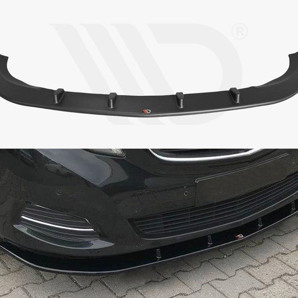 A black car front spoiler with aerodynamic fins is displayed. It is positioned on the front bumper of a black car parked on a cobblestone surface.