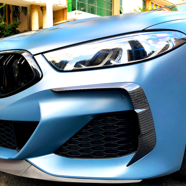 A sleek car front features angular headlights and a sporty grille, parked in an urban environment with modern buildings in the background.