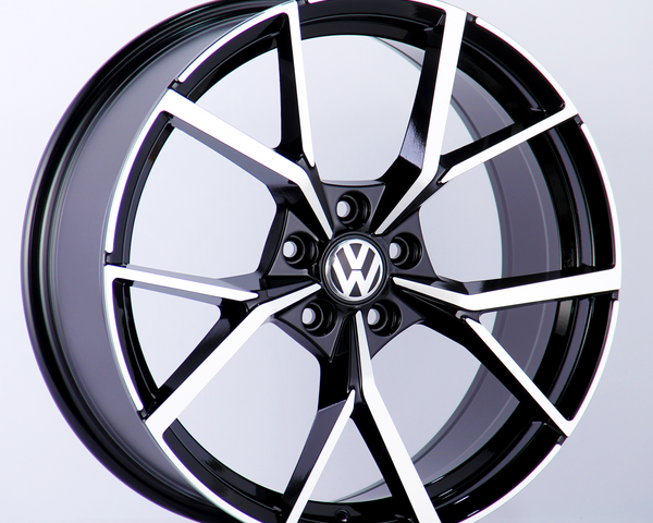A black and silver alloy wheel with a Volkswagen logo in the center is positioned upright against a plain white background, highlighting its intricate spoke design.