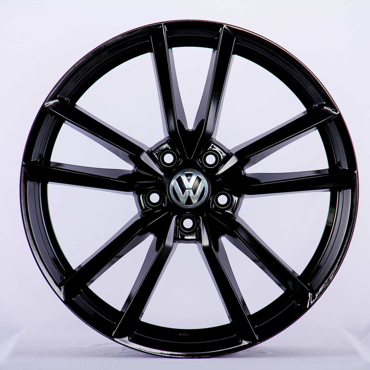 A shiny black car wheel features multiple spokes radiating from a central hub with the Volkswagen logo. It's displayed against a plain white background.