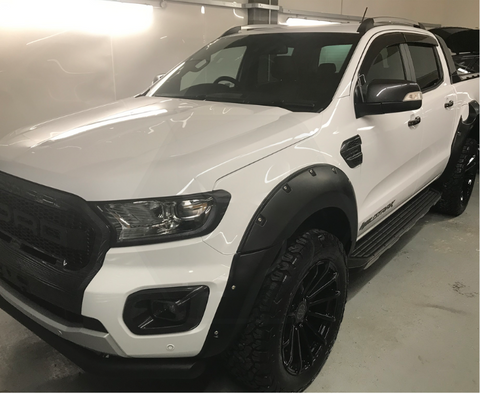 White pickup truck parked indoors, showcasing a robust design with large tires and a black grille. The side has "WILDTRAK" branding. The surrounding environment is a clean garage.