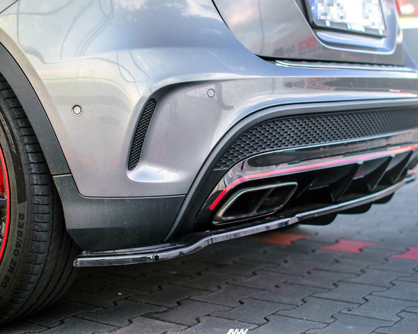 The rear view of a silver car features dual exhaust pipes and red-accented wheels, parked on a cobblestone surface.