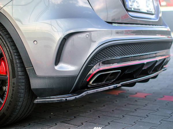 The rear view of a silver car features dual exhaust pipes and red-accented wheels, parked on a cobblestone surface.
