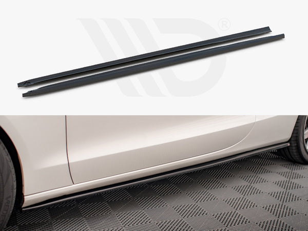 Two long, narrow black side skirt extensions displayed above the side profile of a white car. The car is parked on a textured floor, enhancing its sporty appearance.