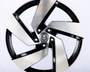 A five-spoke alloy wheel, featuring a polished black and silver design with a central logo, is positioned upright on a plain, light background.