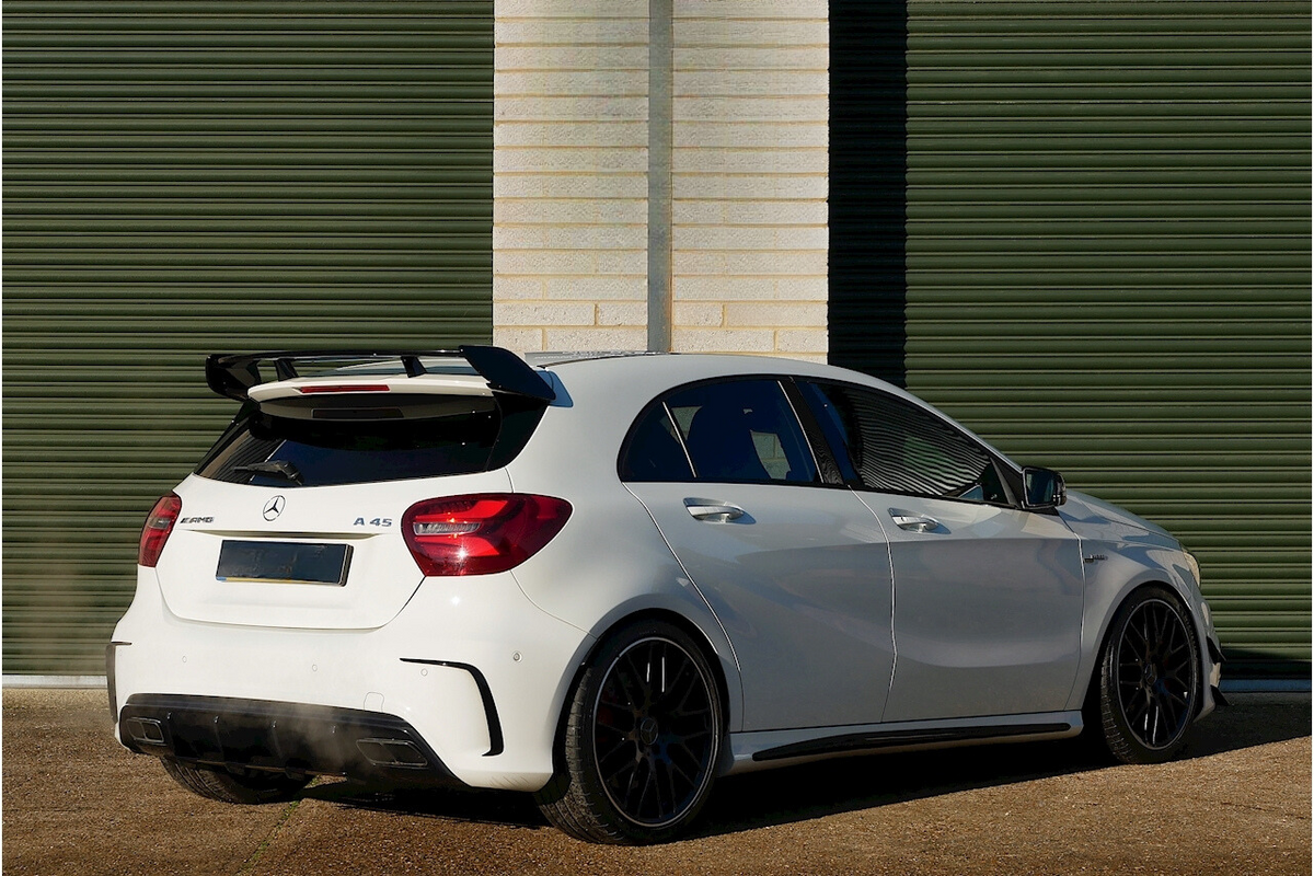 A white Mercedes A45 AMG car is parked outside, featuring a rear spoiler and dual exhausts. It's situated against a background of green horizontal metal shutters.