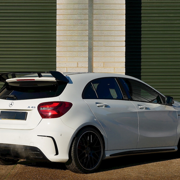 A white Mercedes A45 AMG car is parked outside, featuring a rear spoiler and dual exhausts. It's situated against a background of green horizontal metal shutters.