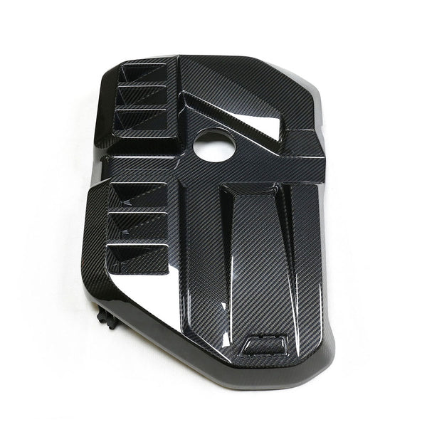 A carbon fiber engine cover with geometric patterns and a circular cutout, placed on a plain white background.