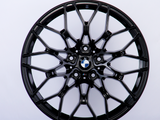 A black, intricately designed car wheel rim with the BMW logo at the center against a plain white background.