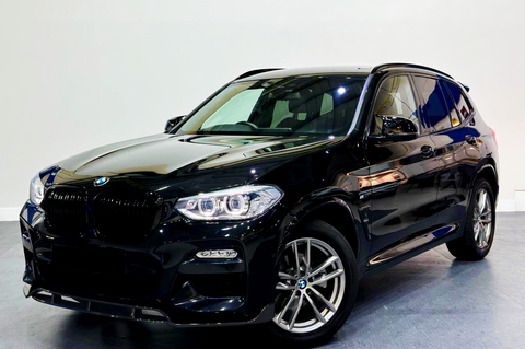 A shiny black SUV is parked indoors, featuring alloy wheels and illuminated headlights, set on a smooth gray floor against a plain white wall.