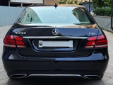 A black Mercedes-Benz E250 CDI is parked on a paved surface between modern buildings, with 