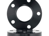 A black circular metal flange with five bolt holes is vertically positioned, placed on another similar flange beneath it against a plain white background.