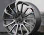 A modern alloy wheel stands upright, displaying intricate split-spoke design. Center hub bearing the text "RANGE ROVER." Positioned in an outdoor, urban setting with a concrete base.