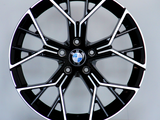 A black and silver alloy wheel with a BMW logo rests vertically on a round white platform against a plain grey background.