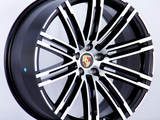 A black and silver alloy wheel with a multi-spoke design featuring the Porsche logo at the center, displayed against a plain white background.