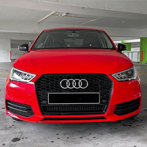 A red Audi car is parked, facing forward, in a multi-level parking garage with concrete walls and a green-painted area.