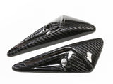 Two carbon fiber objects feature a sleek, aerodynamic design with pointed ends and small circular cutouts, set against a plain white background.