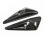 Two carbon fiber objects feature a sleek, aerodynamic design with pointed ends and small circular cutouts, set against a plain white background.