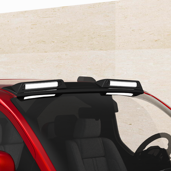 A red car with a roof rack mounted, holding two rectangular lights. The vehicle is parked against a plain, beige wall, seen from a slightly elevated front angle.
