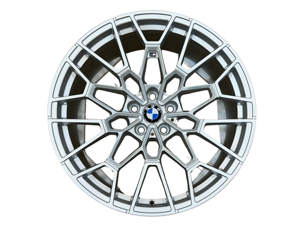 A silver alloy wheel with intricate spoke design, featuring a central blue and white logo, set against a plain white background.