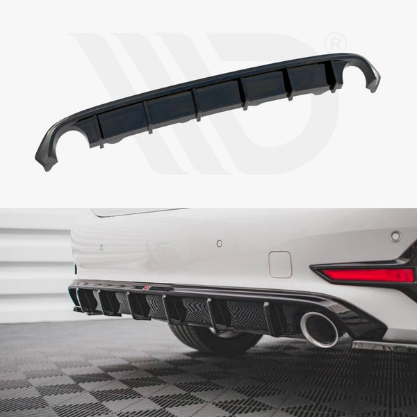 A curved black car diffuser with multiple fins sits in front of a parked white car, enhancing aerodynamics. The car is on a tiled floor within a garage-like setting.