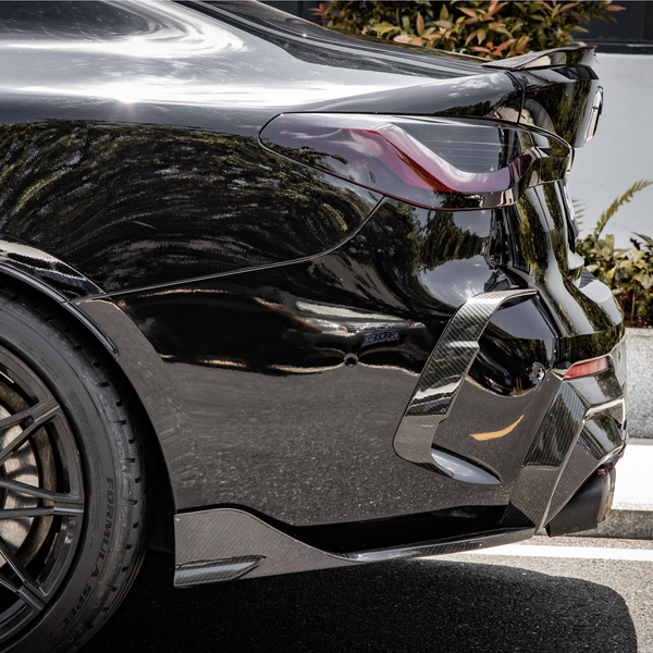 A black car is parked on a street, with sunlight reflecting on its polished surface. It features sleek, curvy design lines and sporty alloy wheels, bordered by greenery and a curb.
