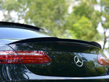A black Mercedes-Benz car is parked outdoors, its rear showcasing a sleek spoiler and distinctive taillights. The green background of trees suggests a serene, natural setting.