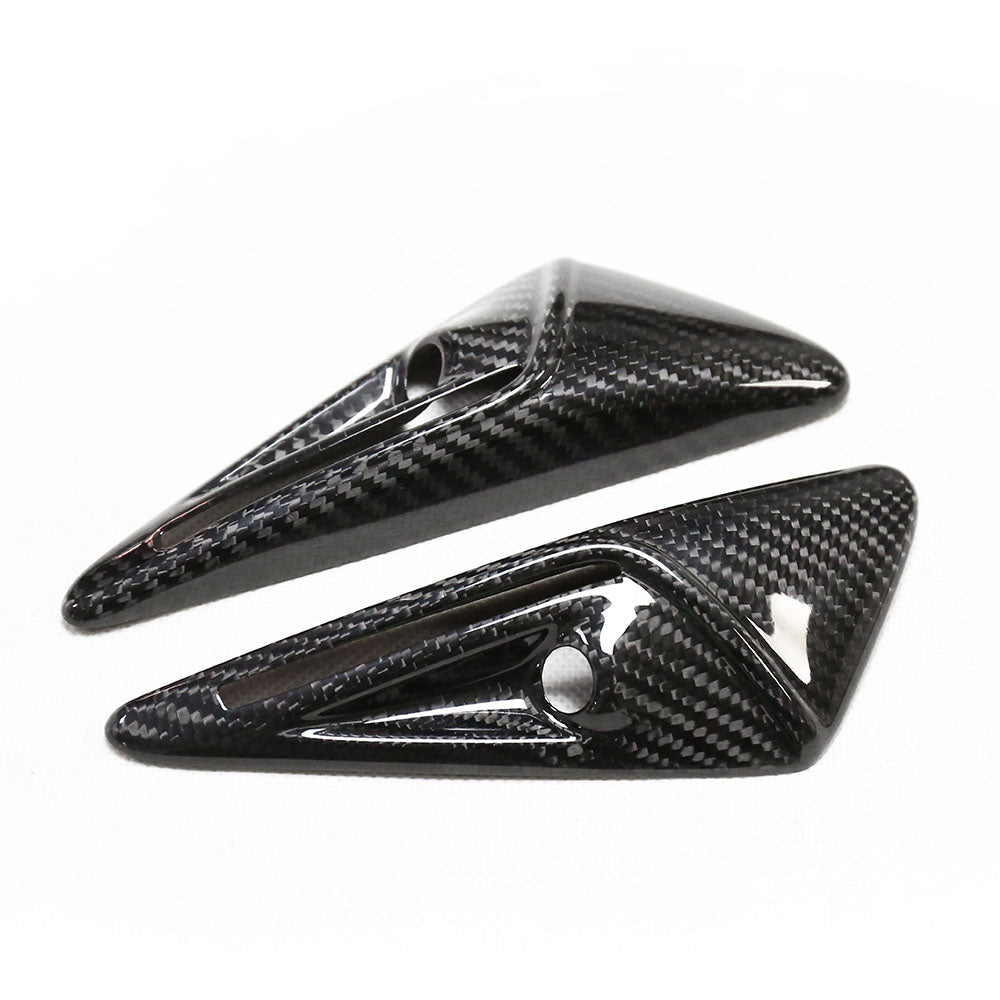 Two glossy, carbon fiber-finished, triangular objects with small circular holes lie angled on a white surface.