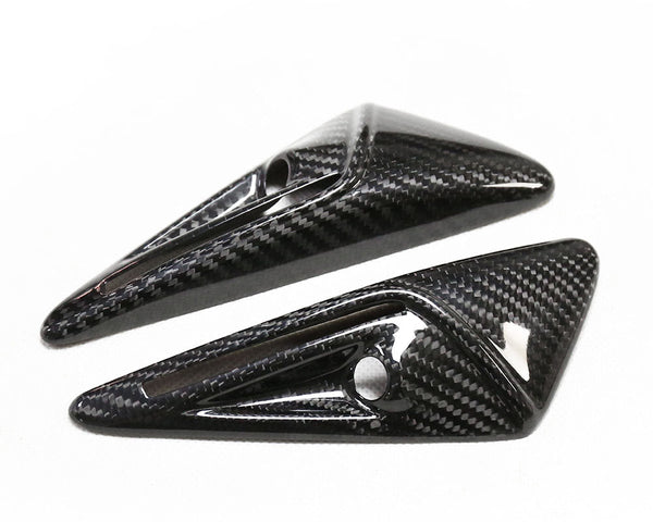 Two glossy, carbon fiber-finished, triangular objects with small circular holes lie angled on a white surface.