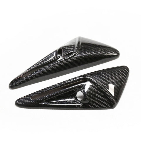 Two glossy, carbon fiber-finished, triangular objects with small circular holes lie angled on a white surface.