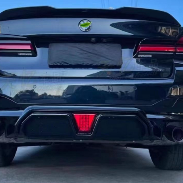 A sleek black car is parked, showcasing dual exhausts and distinctive rear lights, in a sunny outdoor setting with clear blue skies and nearby shrubbery.