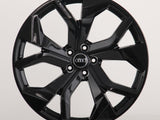 A glossy black car wheel with multiple spokes featuring the Audi logo at its center, displayed against a plain white background.