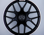 A black Mercedes-AMG wheel with a multi-spoke design stands upright against a gray background. The Mercedes logo is centered, with "AMG" text at the top of the wheel.
