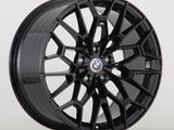A shiny black alloy wheel with a geometric, multi-spoke pattern displays the BMW logo at its center. It rests upright on a plain white background.