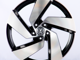 A sleek, silver and black alloy wheel with an intricate design sits upright in a well-lit studio. The central emblem features the Volkswagen logo against a plain white background.