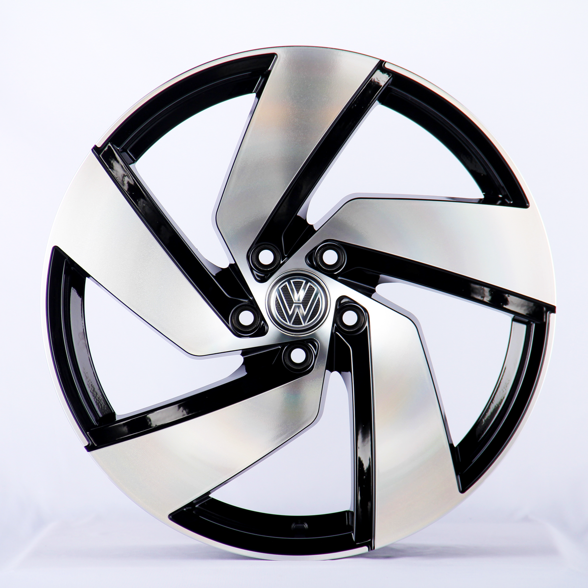 A sleek, silver and black alloy wheel with an intricate design sits upright in a well-lit studio. The central emblem features the Volkswagen logo against a plain white background.