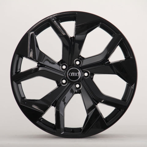 A glossy black car wheel rim with five split spokes, featuring the Audi logo in the center, is displayed against a plain white background.
