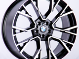 A BMW alloy wheel with a black and silver geometric spoke pattern rests against a white background, featuring the BMW logo at the center.