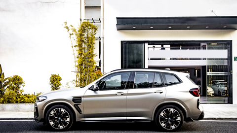 A sleek SUV is parked on a city street, adjacent to a modern building with large windows and labeled "INSTITUTE OF BY CARBON." Tall plants decorate the sidewalk.