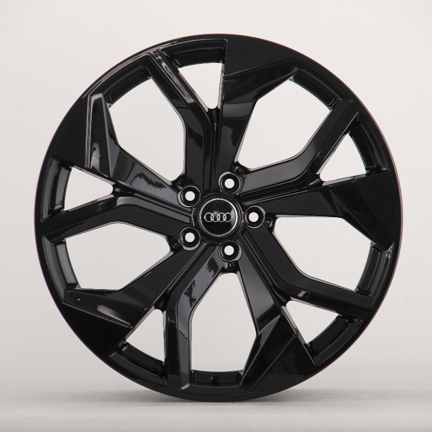 A black, glossy alloy wheel with a five-spoke design, displaying the Audi logo in the center, is positioned against a plain light gray background.