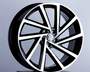 A sleek, modern Volkswagen wheel rim featuring bold geometric spokes is displayed on a black pedestal against a neutral background. It has a glossy black and silver finish with the Volkswagen logo at the center.