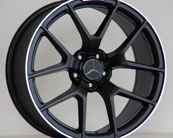 A black alloy wheel with a Mercedes-Benz logo is resting on a wooden surface against a plain background. Text on the rim reads "AMG" with a stylized logo.